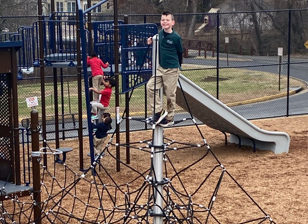 A smiling boy stands on top of a rope-style jungle gym