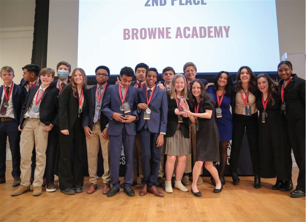 A group of students stand in front of a screen that says '2nd Place Browne Academy'