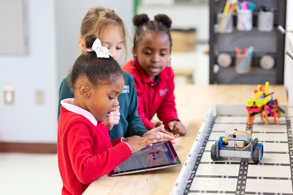 Lower school students use an iPad to code and manipulate a robot.