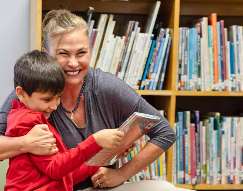 Teacher hugging student reading a book