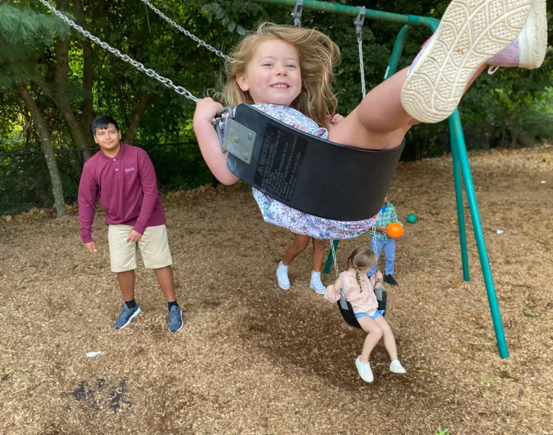a middle schooler pushes his preschool buddy on a swing