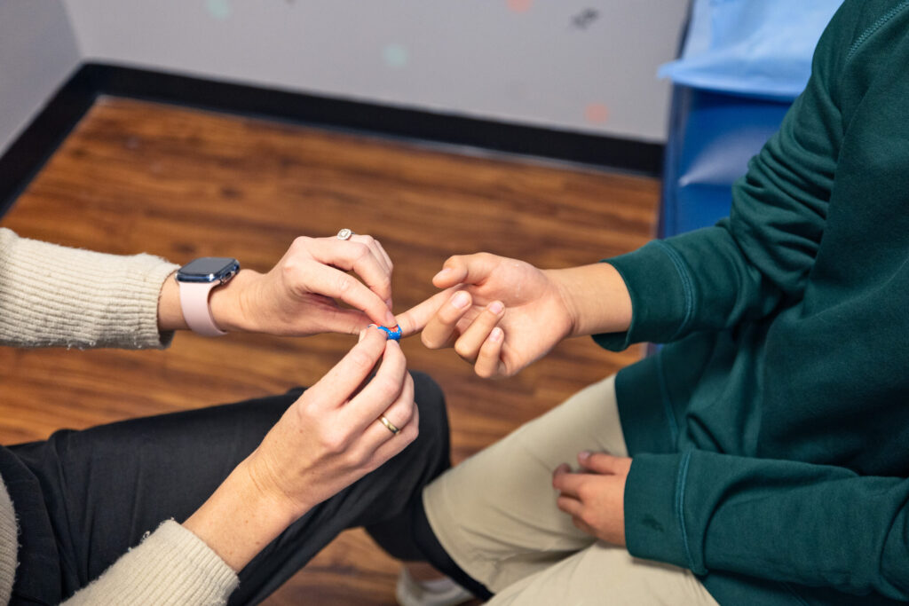A school nurse's hands wrap a blue band-aid around a students finger